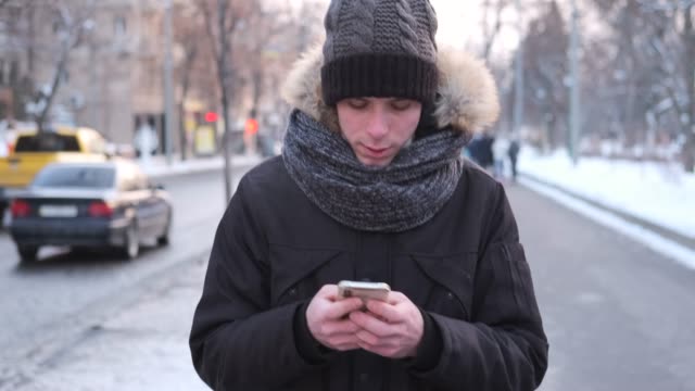 Man-walking-on-street-in-warm-clothing-and-text-messaging-on-mobile-phone