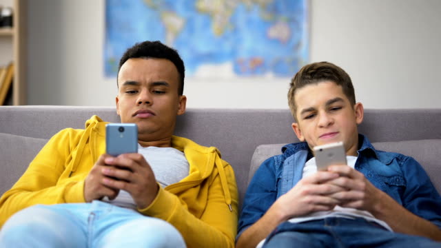 Multiracial-teenage-friends-playing-games-on-smartphones,-ignoring-each-other