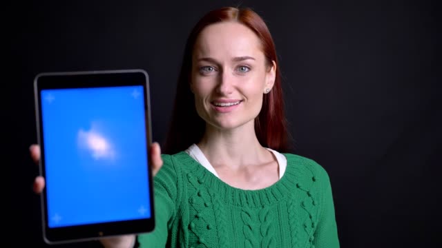 Closeup-portrait-of-attractive-caucasian-female-scrolling-down-on-the-tablet-and-showing-its-screen-to-camera-smiling