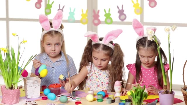Glückliche-Kinder,-die-am-Ostersamstag-hanzige-Ohren-tragen-und-Eier-malen.