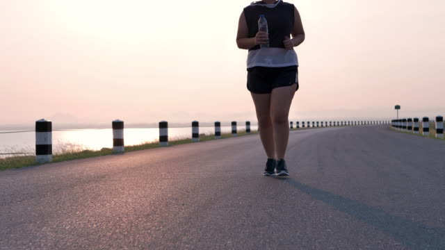 Übergewichtige-asiatische-Frauen-joggen-am-frühen-Morgen-im-Sonnenlicht-auf-der-Straße.-Konzept-des-Gewichtsverlustes-mit-Bewegung-für-die-Gesundheit.-Langsame-Bewegung,-Bottom-Ansicht