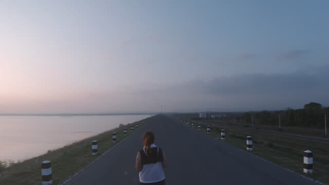 Asiatische-Frauen-joggen-in-der-Straße-am-frühen-Morgen-Sonnenlicht-am-Wasserspeicher-Pa-Sak-Jolasid-Dam.-Konzept-des-Gewichtsverlustes-mit-Bewegung-für-die-Gesundheit.-Langsame-Bewegung,-Rückansicht