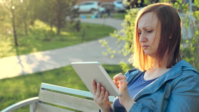 Mujer-usando-tableta-de-ordenador-sentada-en-el-banco-en-la-ciudad