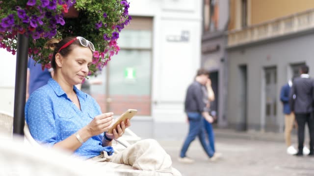 Junge-Frau-sitzt-im-Straßencafé-auf-der-Terrasse-und-benutzt-ihr-Smartphone.