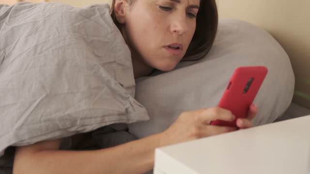 Woman-waking-up-and-using-mobile-phone-in-bed