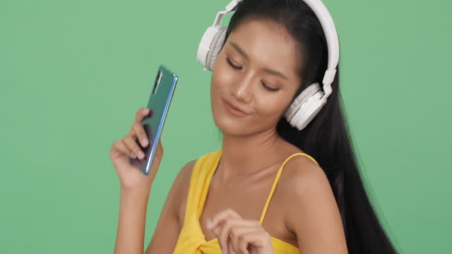 Asiatische-schöne-Frau-hören-Musik-online-und-glücklich-Emotion-Lächeln.-Frau-trägt-Kopfhörer-und-halten-Smartphone.-Konzept-von-Schönheit,-Mode-und-Musikerlebnis.