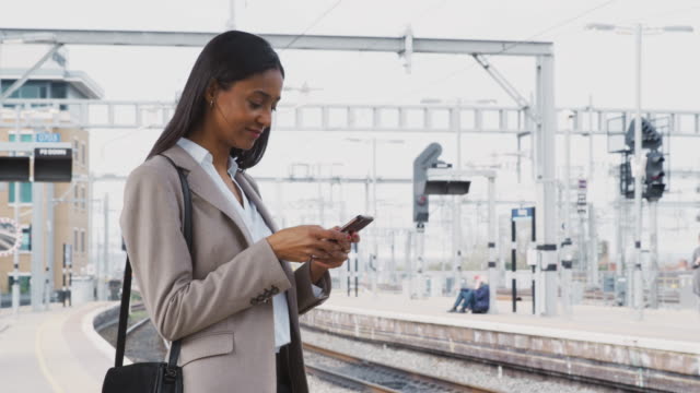 Empresaria-que-se-comunica-para-trabajar-de-pie-en-la-plataforma-del-tren-usando-el-teléfono-móvil