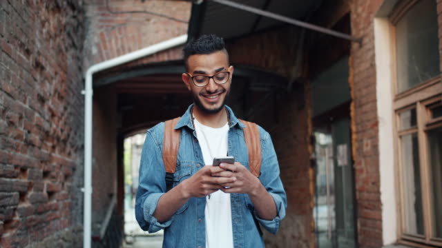 Cámara-lenta-de-estudiante-árabe-usando-teléfono-inteligente-y-riendo-de-pie-al-aire-libre