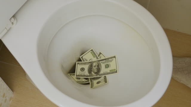 Desperdicio-de-dinero.-La-mano-tira-billetes-de-dólares-en-el-baño.-Closeup