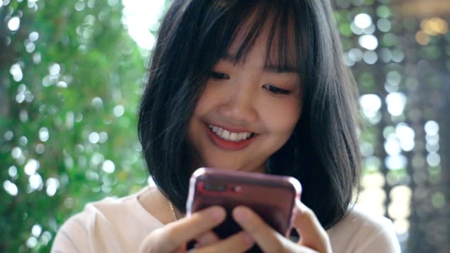 Junge-asiatische-Frau-mit-Blick-auf-mobiles-Smartphone