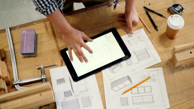 Male-hand-touching-tablet-screen-with-technical-drawing-of-furniture-in-workshop