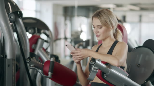 Fitness-mujer-relajarse-con-el-teléfono-móvil-en-el-gimnasio-deportivo.