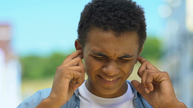 Teenage-boy-closing-ears-from-pain,-suffering-buzzing-noise,-hearing-damage