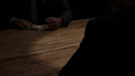 Dishonest-businessman-giving-money-to-partner-at-meeting-in-dark-room