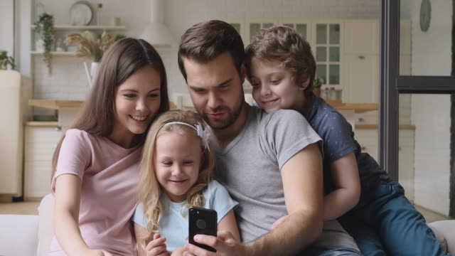 Glückliche-Eltern-mit-Kindern,-die-Spaß-mit-dem-Smartphone-zu-Hause-haben