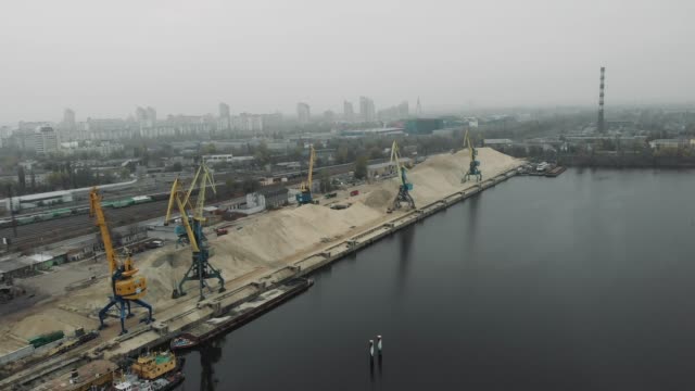 Port-working-cranes-extracting-sand-from-barge-and-scow-in-docks-on-river-bank.-Extraction-of-river-sand-in-docks-of-industrial-city