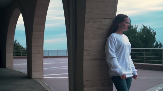 Beautiful-girl-with-long-hair-and-a-white-sweatshirt,-standing-under-one-of-several-arches-of-the-building.