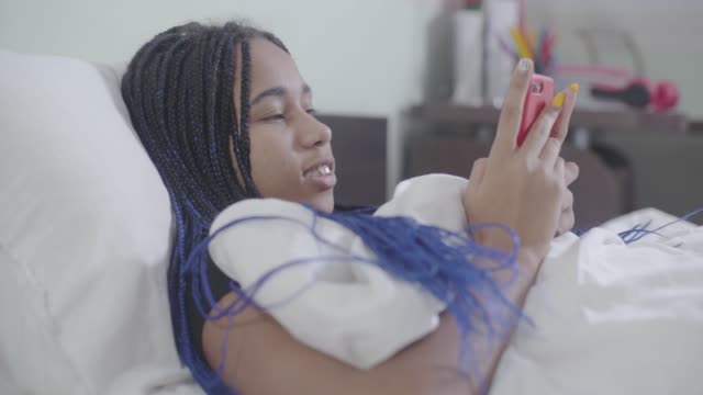 Porträt-von-afroamerikanischen-Mädchen-mit-Dreadlocks-liegen-im-weißen-Bett-und-mit-Smartphone.-Junge-Frau-surfen-Internet-in-der-Nacht.-Social-Media-Sucht,-Lebensstil.