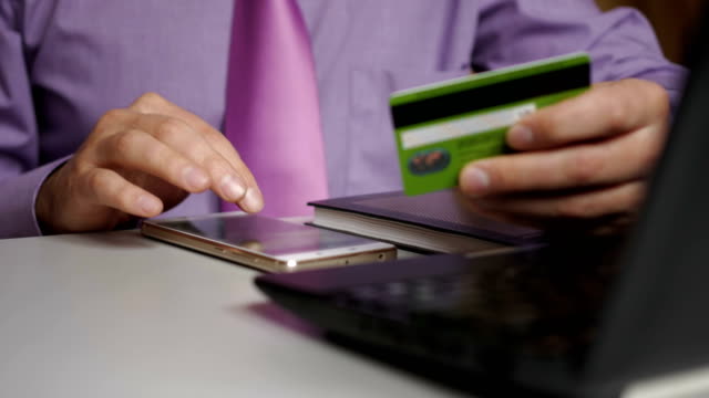 Un-hombre-de-negocios-con-camisa-y-corbata-morada-está-haciendo-un-pago-a-la-banca-por-Internet.-Compras-online-con-tarjeta-de-crédito-en-smartphone.