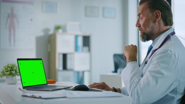 Hausarzt-macht-einen-Videoanruf-mit-Patient-auf-einem-Computer-mit-green-Screen-Display-in-einer-Gesundheitsklinik.-Assistant-in-Lab-Coat-spricht-über-Gesundheitsprobleme-im-Krankenhausbüro.