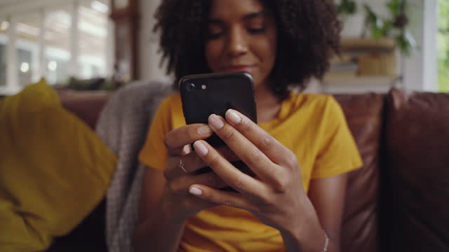 Shot-of-young-woman-sitting-on-sofa-holding-mobile-in-her-hand-checking-messages
