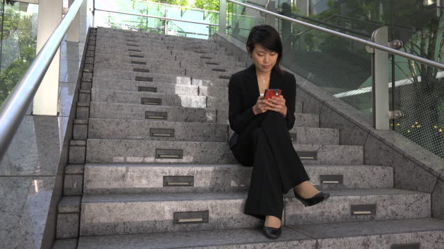 Entspannen-Sie-sich-für-asiatische-geschäftsfrau-SMS-mit-Smartphone-sitzt-auf-der-Treppe