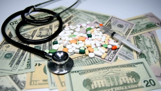 Pills-and-capsules-on-dollars,-with-stethoscope-and-syringe.-Health-care-costs-concept.-Slow-motion.