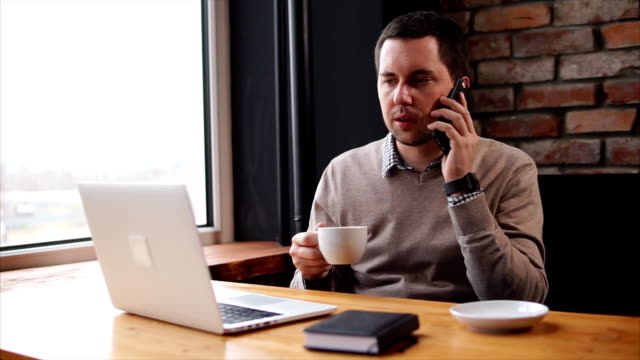 Der-Mann-am-Telefon-sprechen-und-Blick-auf-den-Laptop-während-der-Pause-im-café