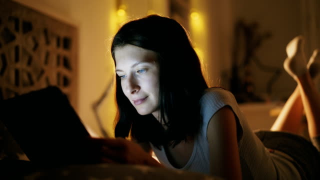 Close-up-of-young-attractive-woman-using-tablet-computer-at-night-time-lying-in-bed-at-home