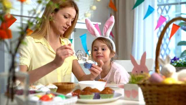 Junge-Mutter-und-ihre-kleine-Tochter-tragen-lustige-Hasenohren-Kochen-Oster-Muffins