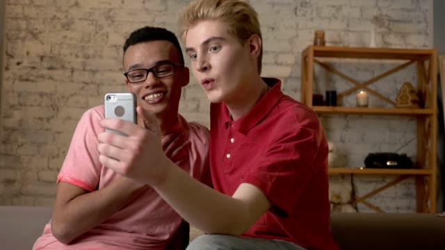 Two-multi-national-friend-of-a-homosexual-watching-cute-pictures-on-a-smartphone.-Internet,-technology,-social-networks-concept.-60-fps