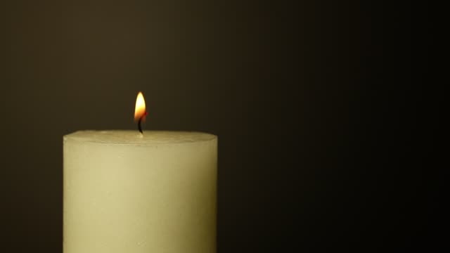 Close-up-white-candle-trembling-flame-over-black