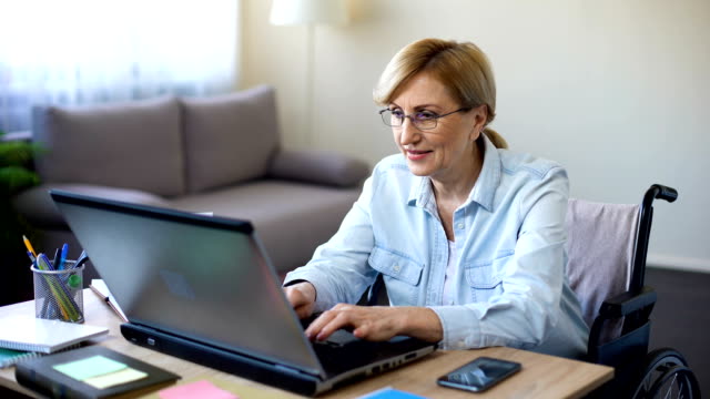 Successful-senior-woman-in-wheelchair-working-on-laptop,-chatting-with-client