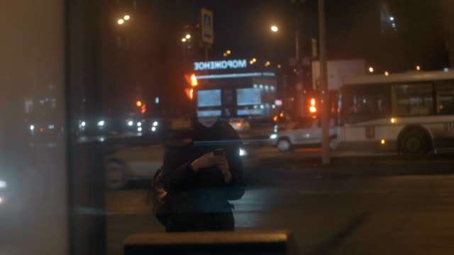 Frau-mit-Zelle-an-Bushaltestelle-in-Nacht-Stadt