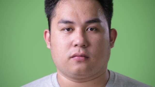 Young-handsome-overweight-Asian-man-against-green-background