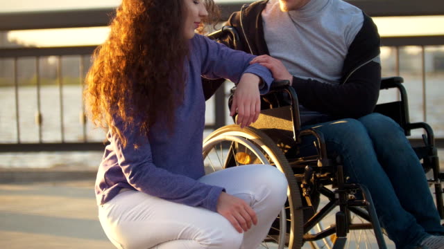 Glückliches-Paar---behinderte-Menschen-im-Rollstuhl-im-Gespräch-mit-attraktiven-jungen-Frau-Enjoing-den-Sonnenuntergang
