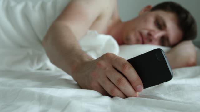 Young-adult-man-lies-on-a-bed-and-uses-phone---feet-level