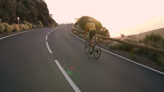 Radfahrer-sitzen-auf-einem-Fahrrad-auf-einem-Smartphone-für-social-Networking-Berglandschaft-bei-Sonnenuntergang-fotografieren.-Slow-motion