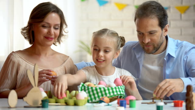 Beautiful-family-putting-dyed-Easter-eggs-into-basket,-Christians-traditions
