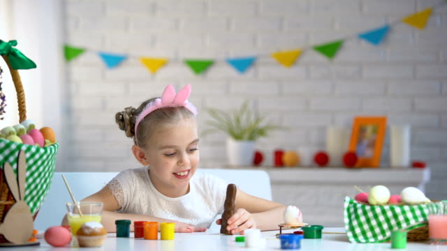 Little-girl-in-cute-headband-smiling-and-posing-at-camera-with-chocolate-bunny