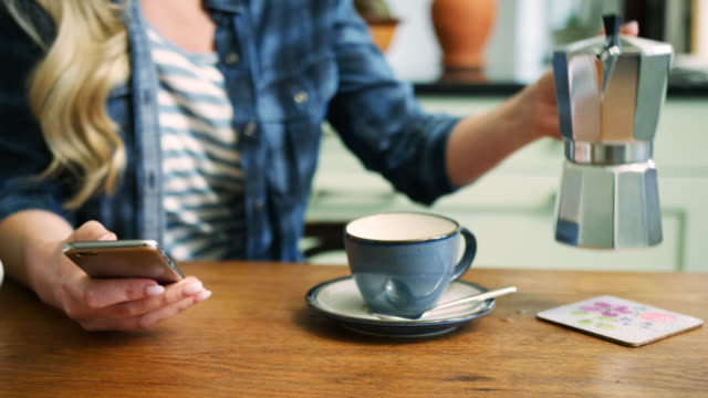Frau-SMS-beim-Ausgießen-Kaffee-am-Frühstückstisch