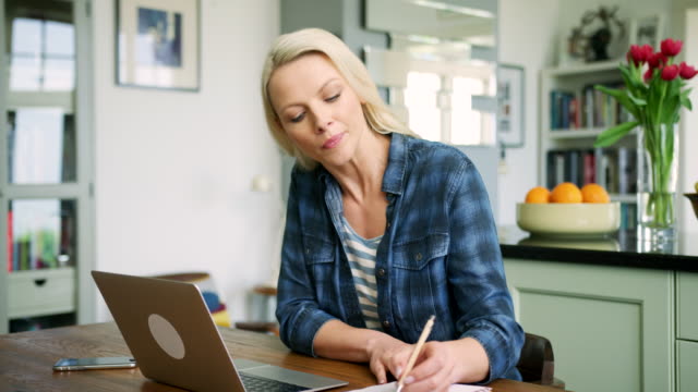 Attractive-Blond-Woman-Typing-On-Laptop-And-Writing-Notes