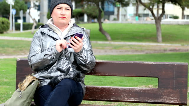 Woman-sitting-on-a-park-bench-with-smartphone