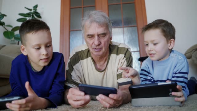Granddad-and-grandchildren-play-on-tablet-in-internet-game-in-room.