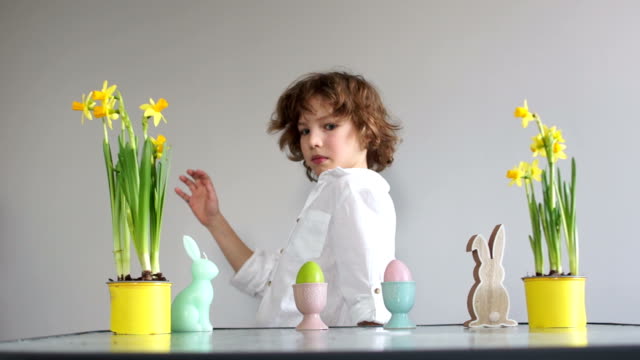 Boy-steals-an-Easter-egg,-childish-pranks.-Curly-cute-schoolboy-near-the-table-with-Easter-decor.-Easter-traditions