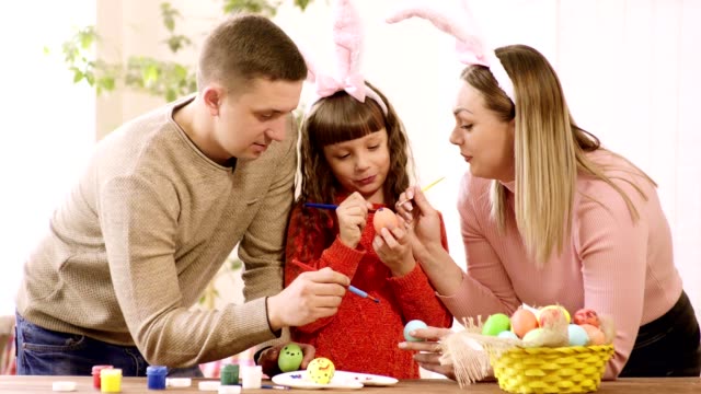 mamá-y-su-hija-en-las-orejas-de-conejo-y-papá-decoran-los-huevos-para-las-vacaciones-de-Pascua.