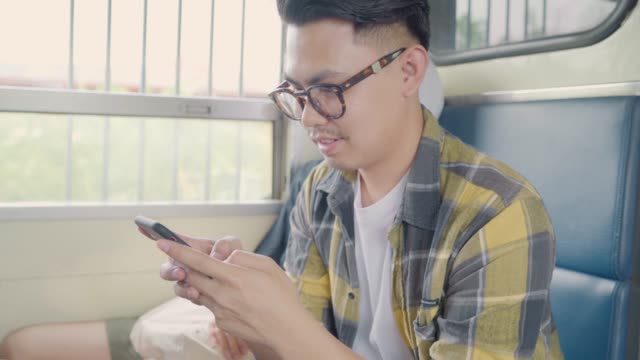 Viajero-asiático-hombre-usando-teléfono-inteligente-comprobando-las-redes-sociales-mientras-toma-un-tren.
