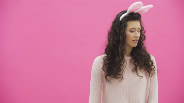 Beautiful-young-girl-standing-on-a-pink-background.-During-this,-there-are-ears-of-rabbits-on-the-head.-Performs-rabbits-rhythmic-movements-with-the-hands-of-a-call.