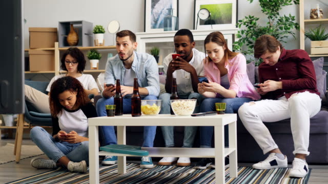 Fröhliche-Freunde,-die-Smartphones-benutzen,-dann-fernsehen-und-diskutieren-Nachrichten