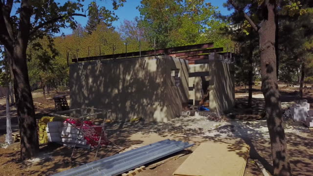 Aerial-shot-of-single-cocrete-building-at-construction-site-in-the-forest.-Camera-flies-towards-the-house-and-building-materials.-Quadcopter-drone-flies-away-from-plastered-toilet-in-park